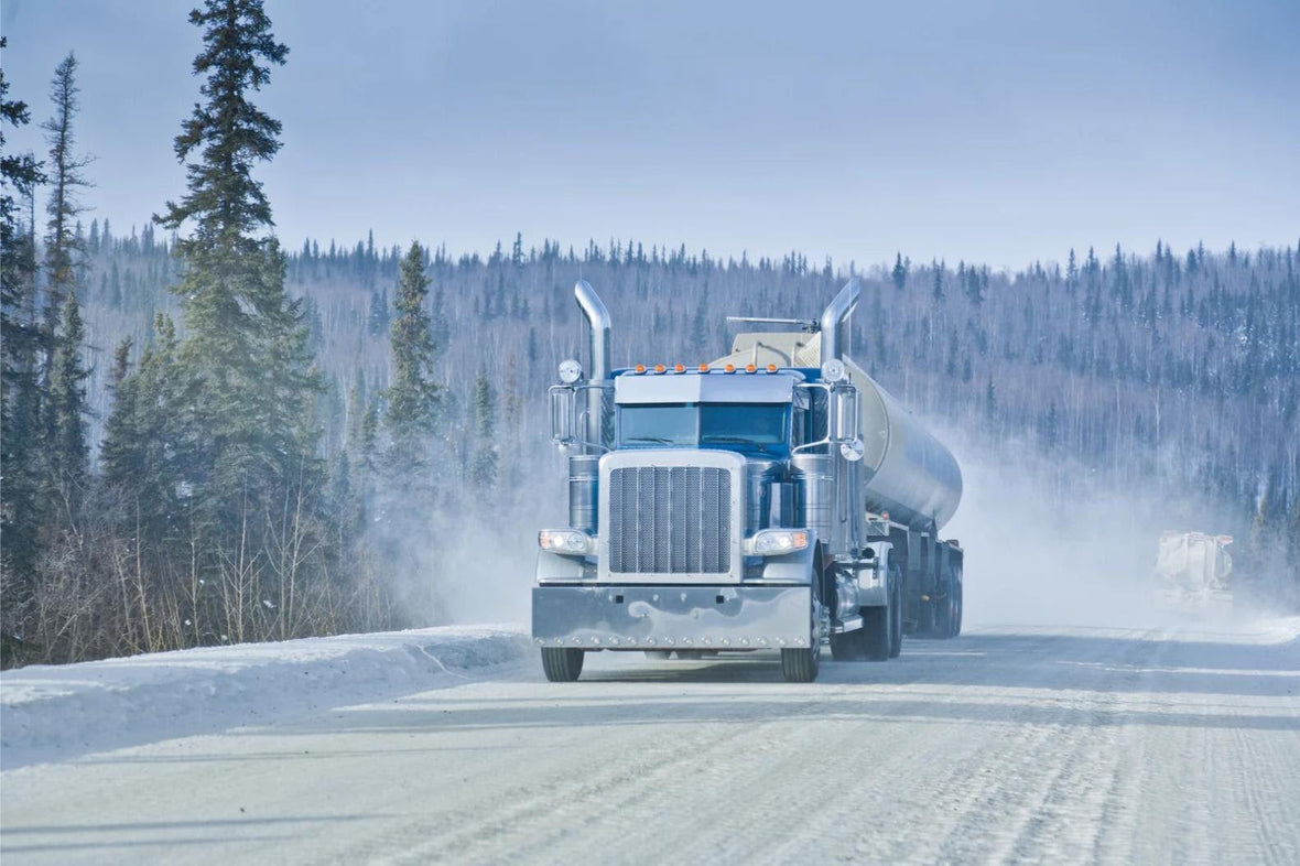 semi truck driving on a snowy road in a forest